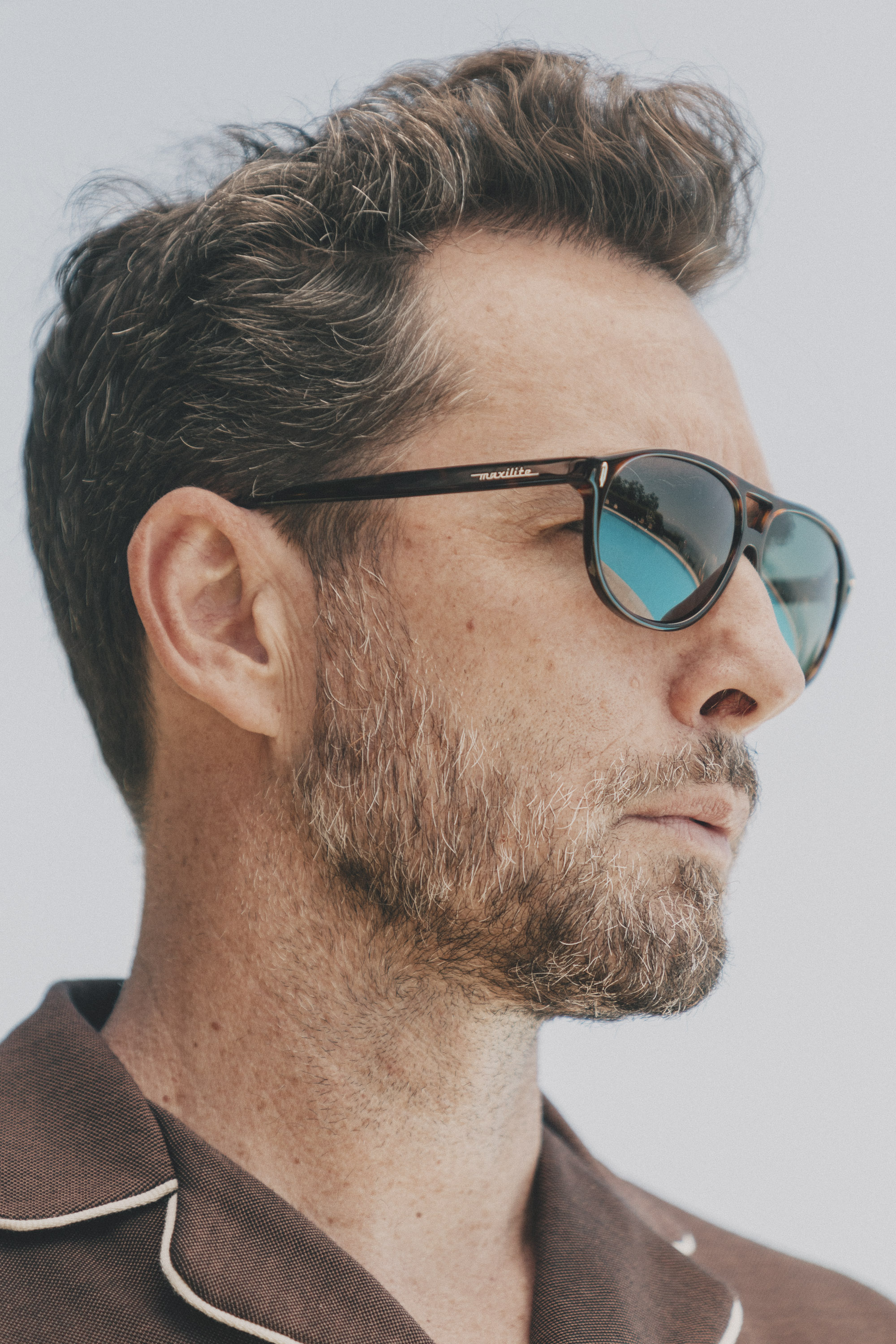 Elegant man in casual look wearing brown sunglasses in retro design and brown polo shirt with white stripe